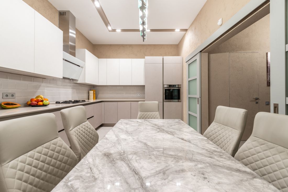 Cuisine beige et blanche ouverte sur une table en marbre