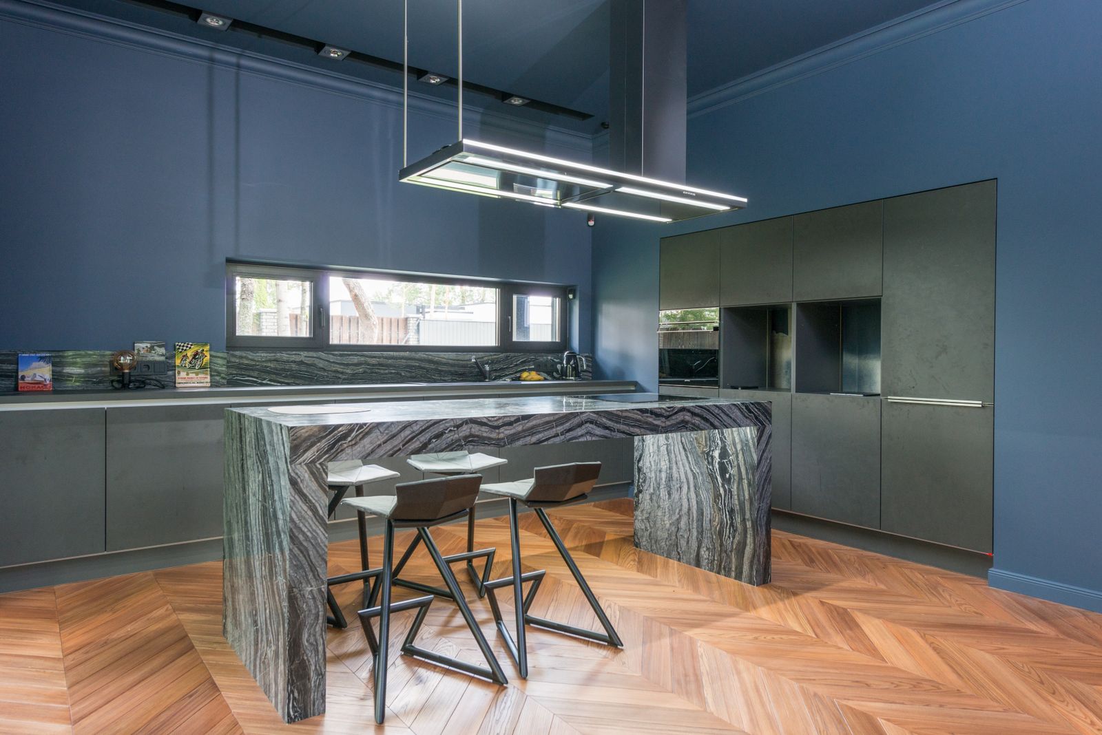 Cuisine bleu nuit avec îlot en pierre veinée et parquet en chevrons